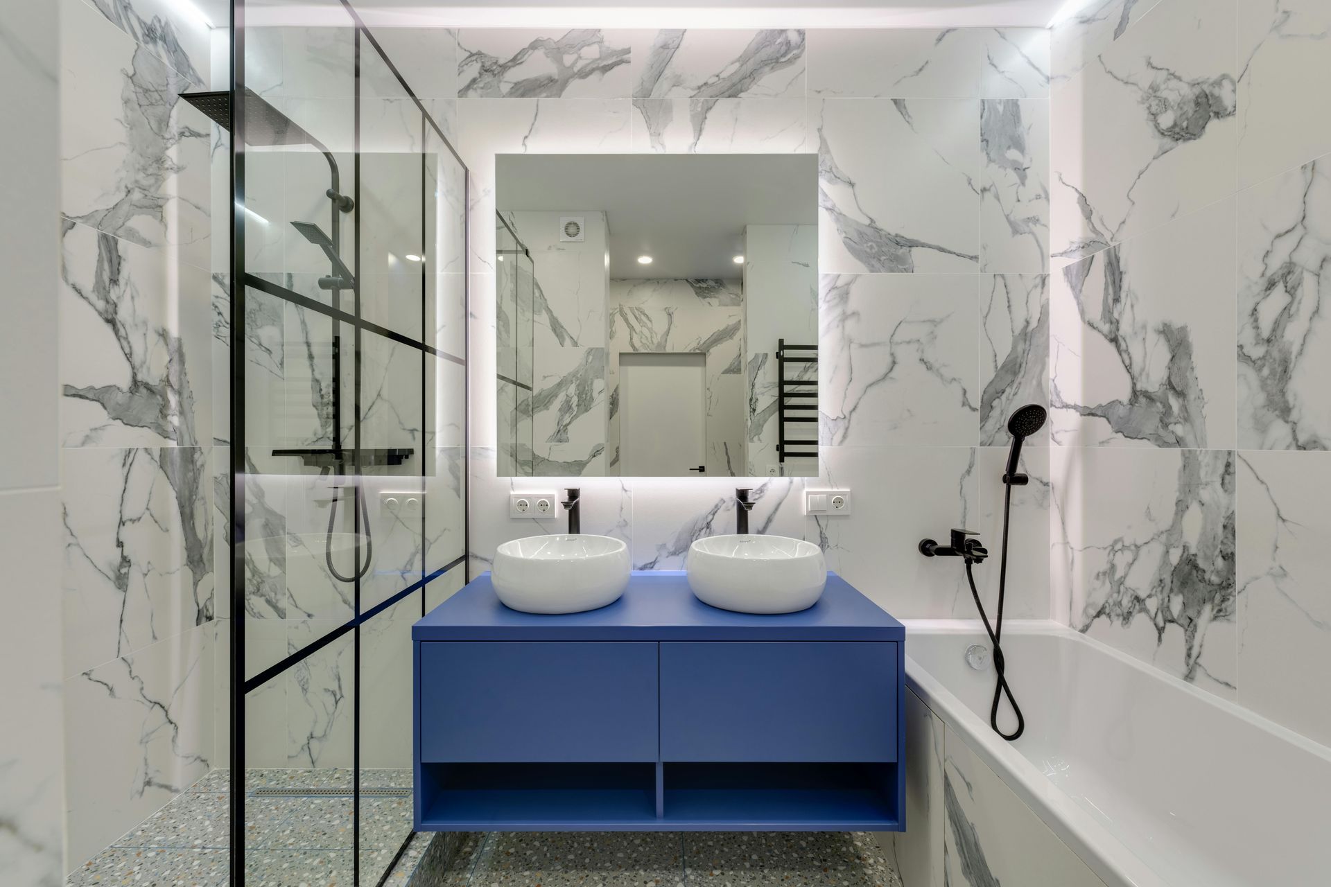 Modern bathroom with blue vanity, marble walls, shower, and bathtub.
