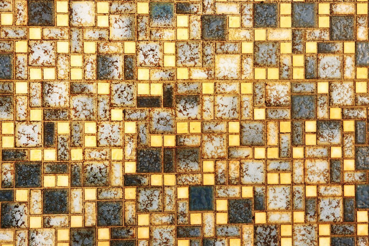 Mosaic tile wall, featuring gold and blue-grey squares and rectangles, with aged appearance.
