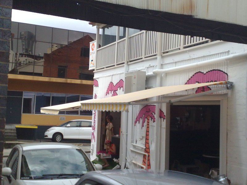 White Car is Parked in Front of a Building With Palm Trees Painted on It — Blind Outfitters in Atherton, QLD