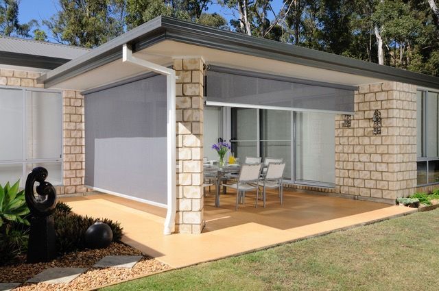 Patio with one grey awning pulled down and other grey awning lifted to reveal table and chairs being shaded — Blind Outfitters in Atherton, QLD