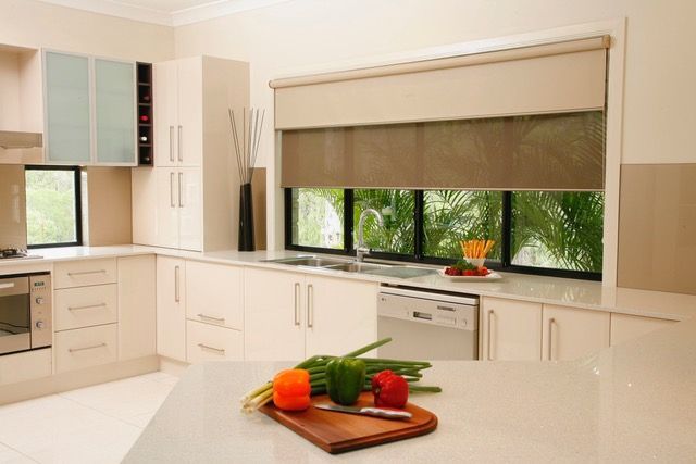 Light filled modern kitchen with food on chopping board on the bench and blinds over the window — Blind Outfitters in Atherton, QLD
