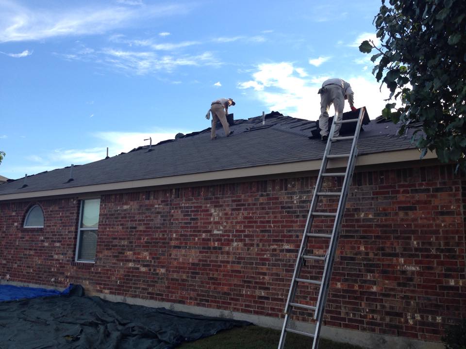 Two men are working on the roof of a brick house