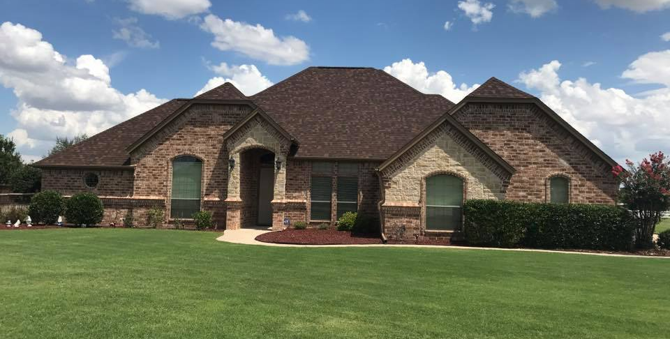 A large brick house with a brown roof is sitting on top of a lush green lawn.