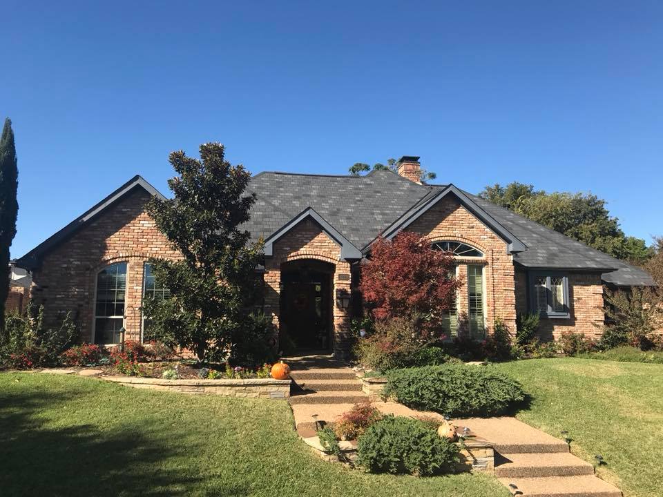 A large brick house with a gray roof is sitting on top of a lush green lawn.