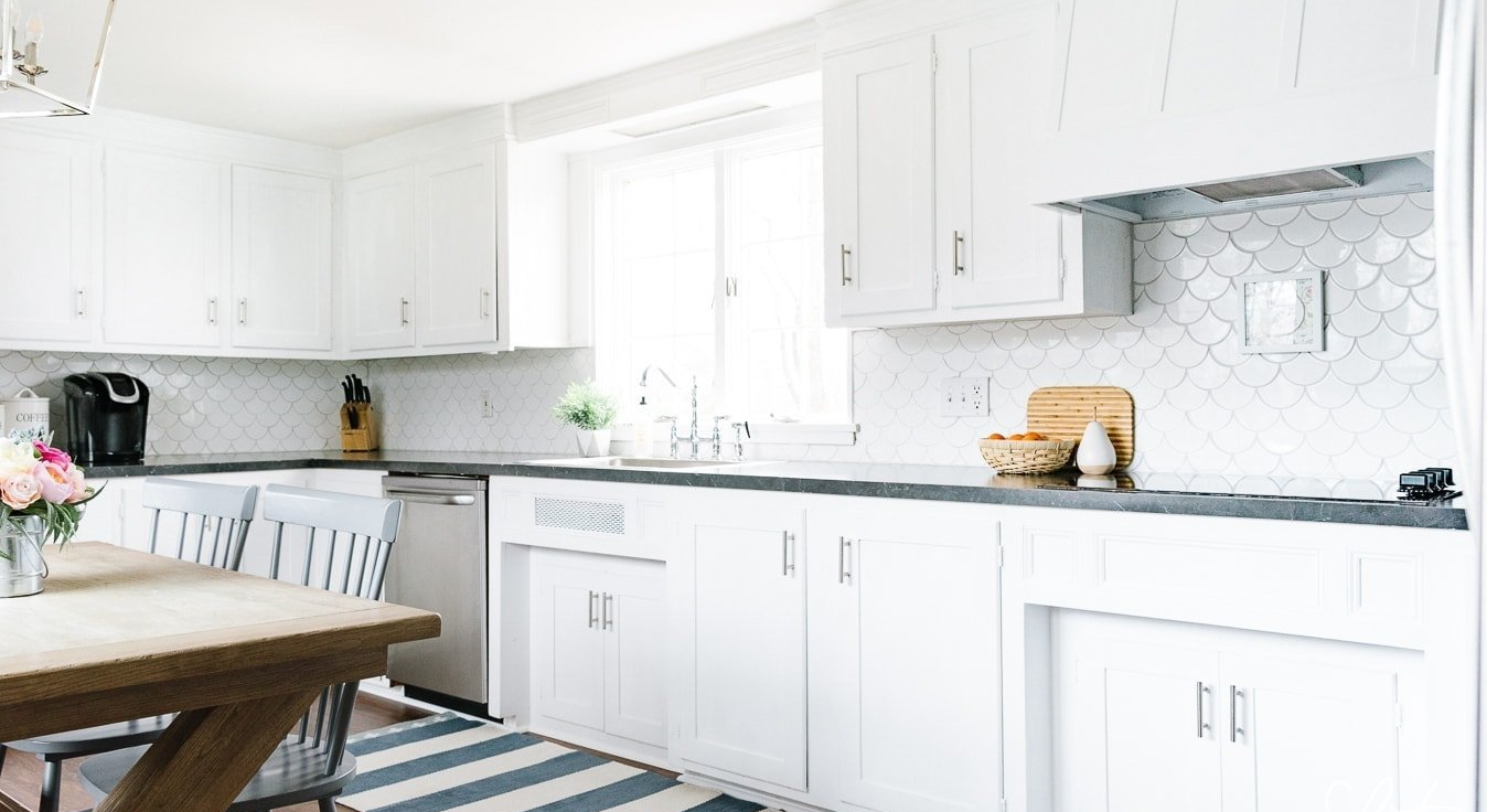 A kitchen with white cabinets and a wooden table and chairs.