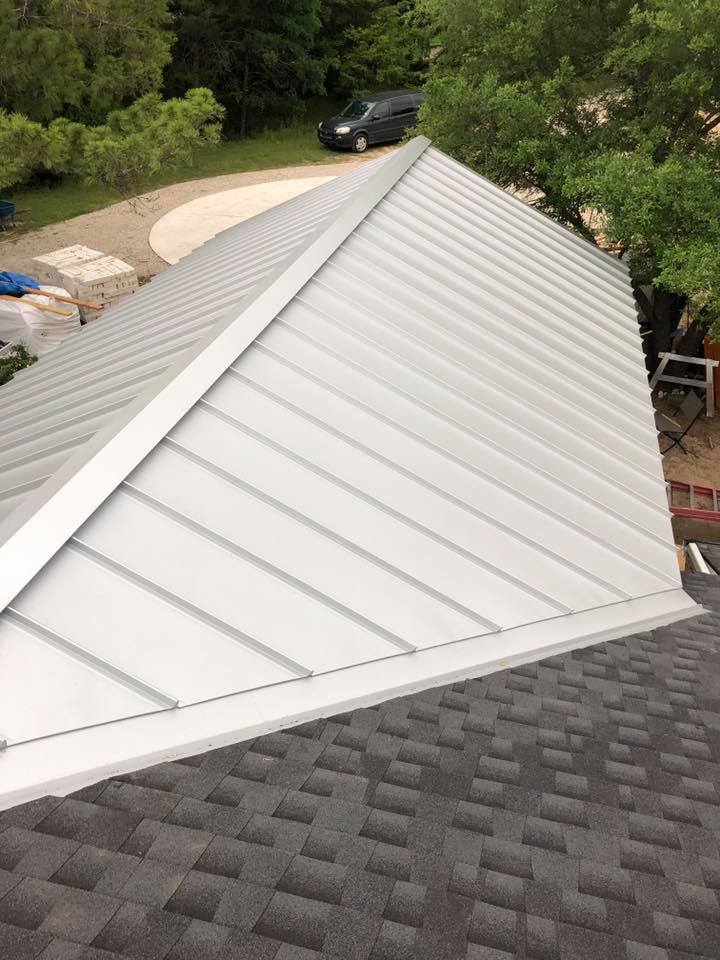 A white metal roof with a black shingle roof is being installed on a house.