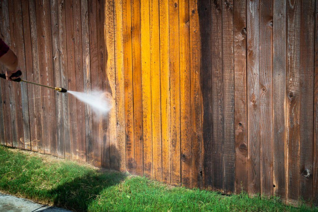 A person is using a high pressure washer to clean a wooden fence.
