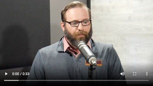 A man with a beard and glasses is speaking into a microphone