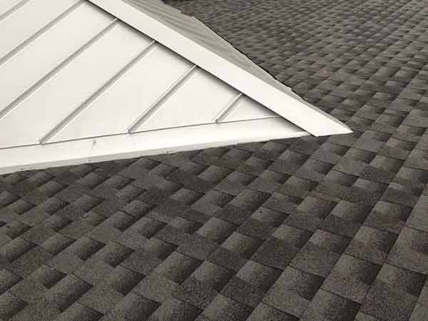 A close up of a roof with a white metal roof and a black shingle roof.