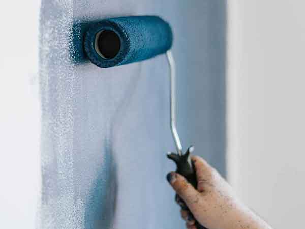 A person is painting a wall with a blue paint roller.