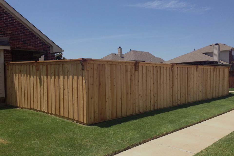 A wooden fence surrounds a lush green yard in front of a brick house.