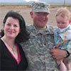 A man in a military uniform is holding a baby and posing for a picture with a woman.