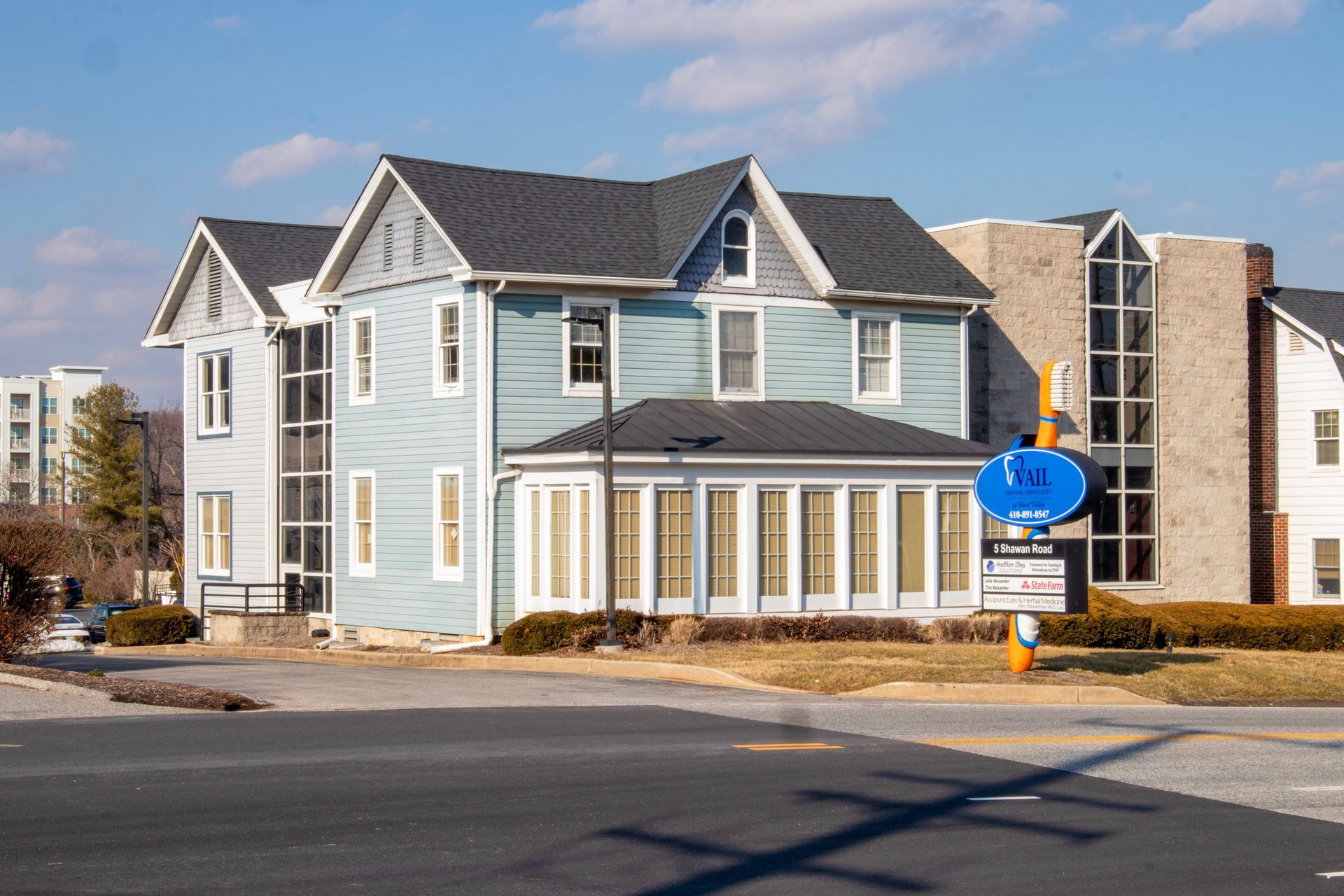 A two-story light blue house with a modern stone addition, next to a street with a sign for