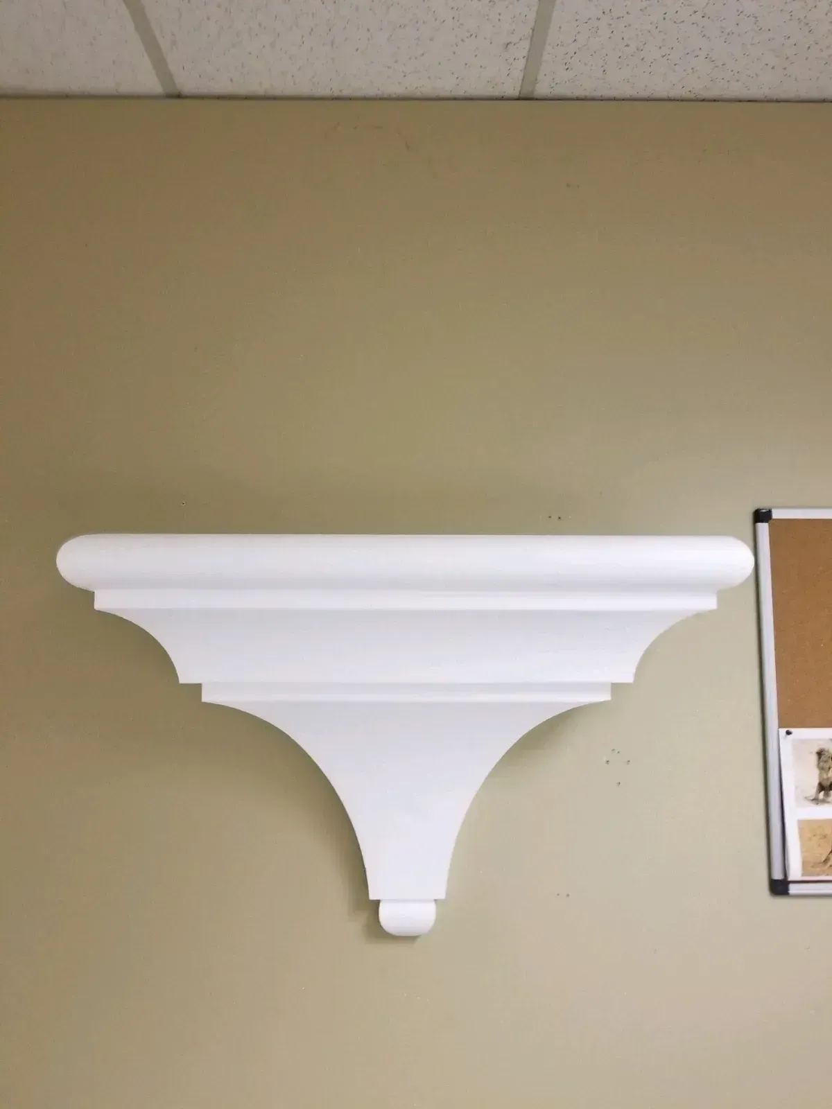 White decorative wall shelf mounted on a beige wall, with a curved, tiered design