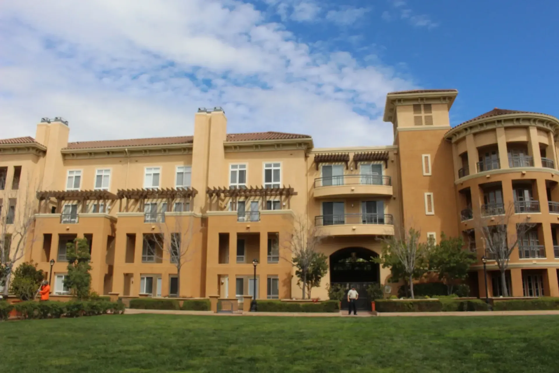 Modern tan apartment building with balconies and green lawn under a blue sky