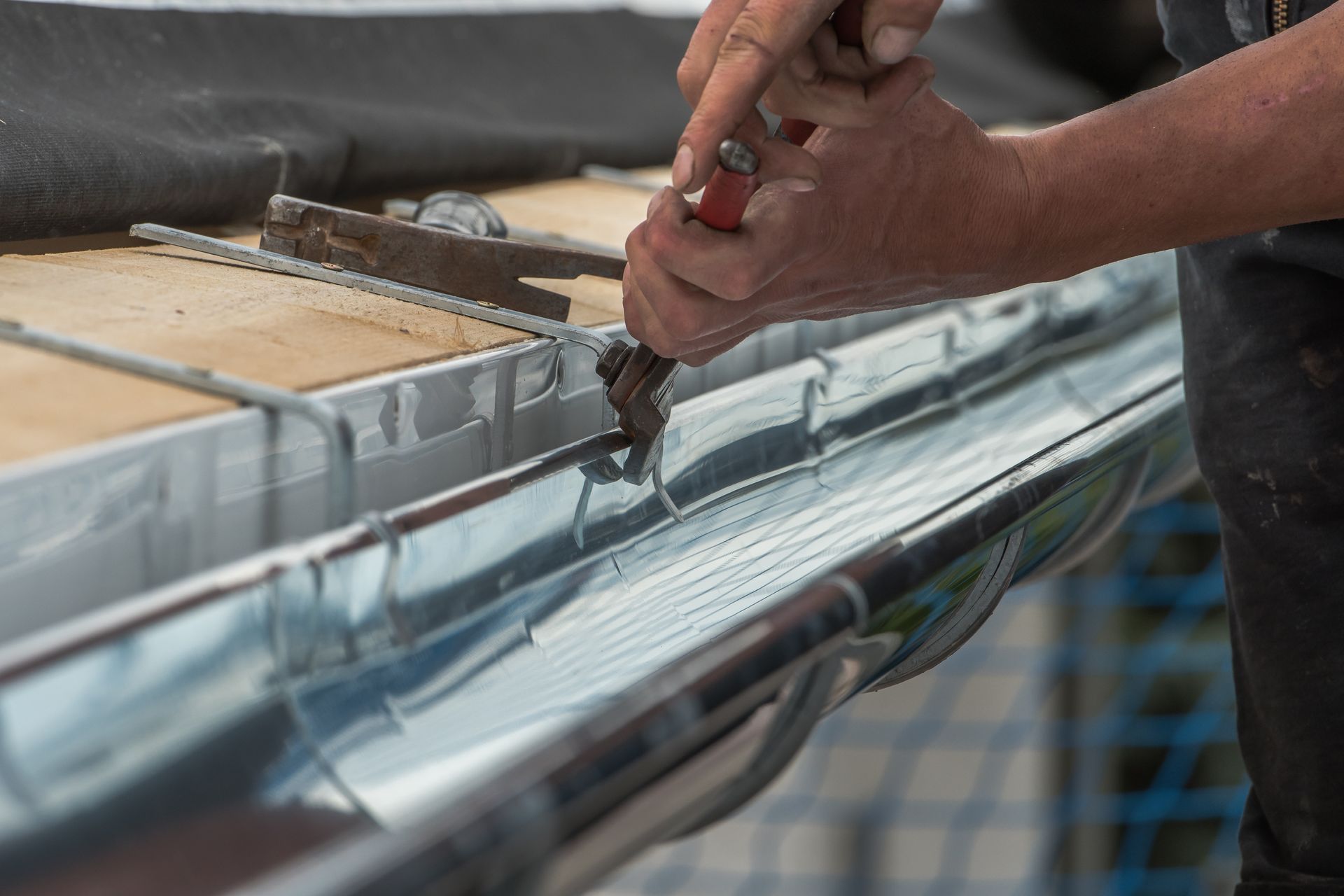 A person is working on a metal gutter with a saw.