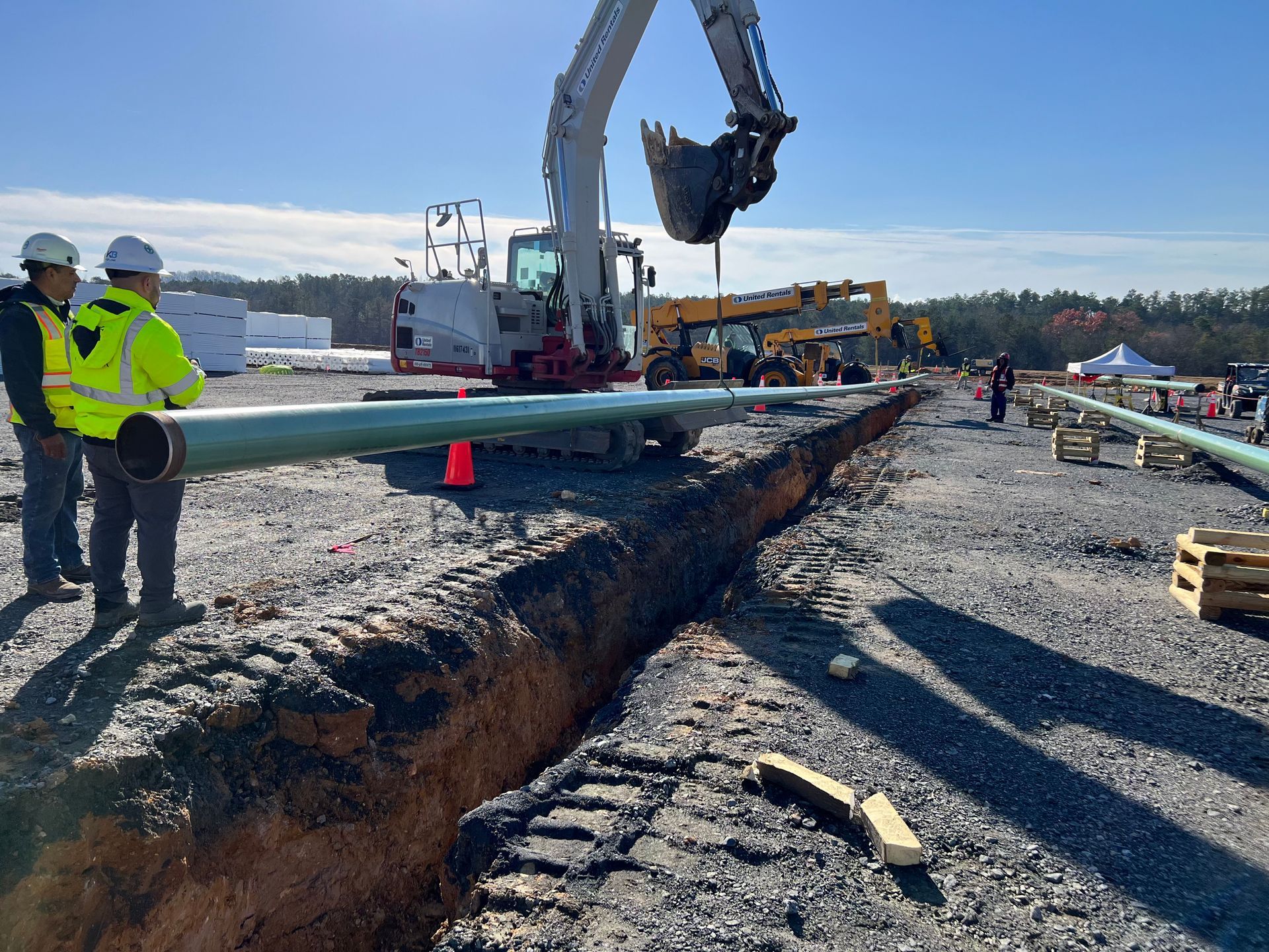 A green pipe is sitting in the dirt next to a pile of gravel.