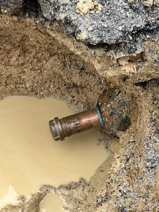 A copper pipe is sticking out of the ground in a puddle of water.