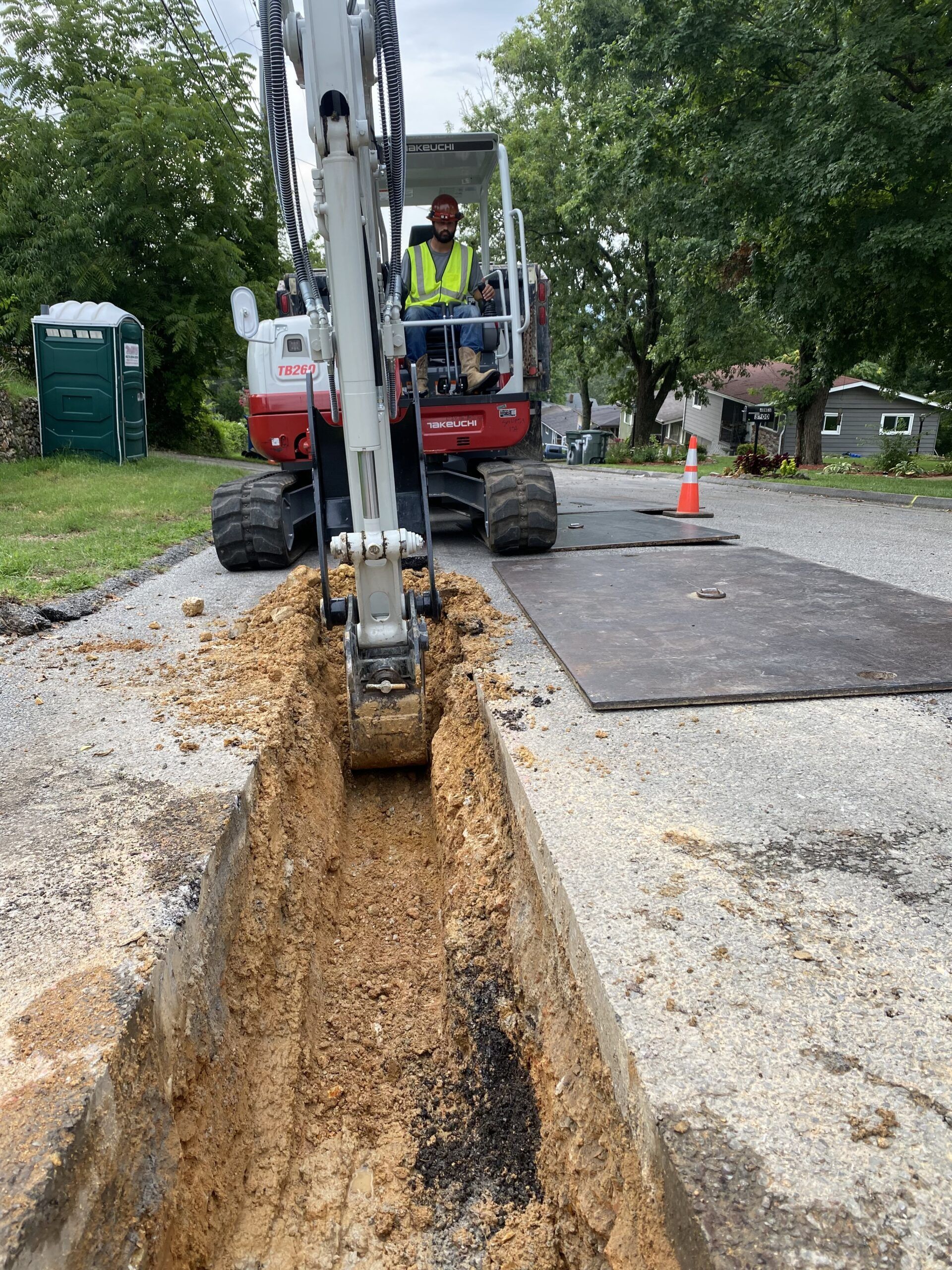 A man is driving an excavator down a dirt road.