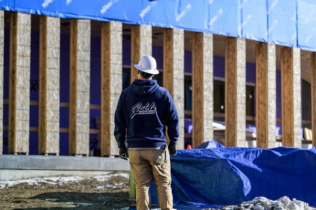 Construction worker wearing a hard hat, facing a building under construction; wood framing, blue tarp.