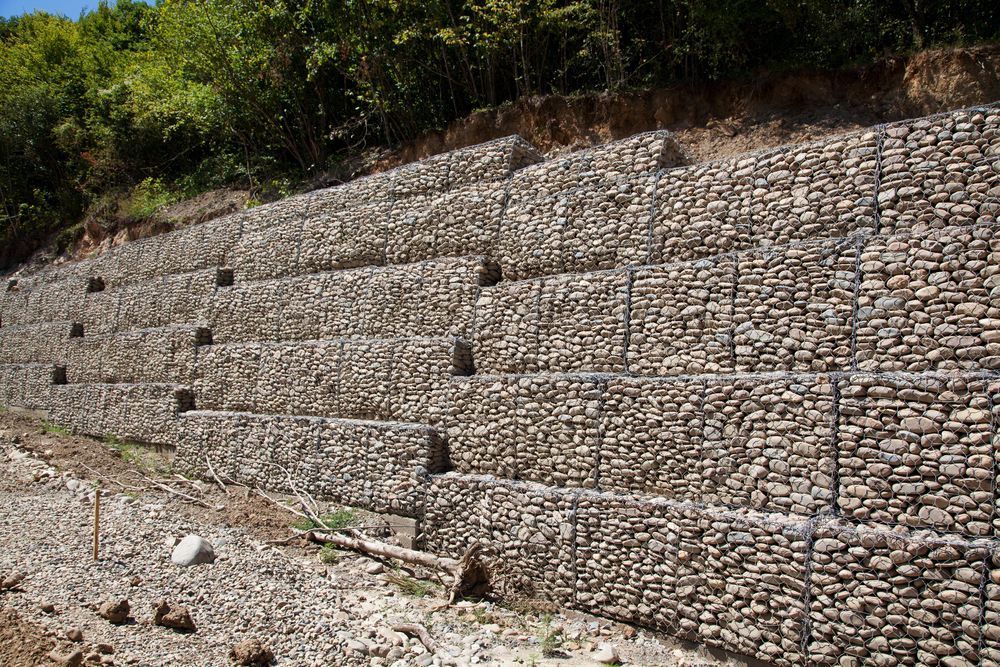 Stone-filled gabion retaining wall on a hillside, supporting earth — Carl Whelan Building & Renovations In Morisset, NSW