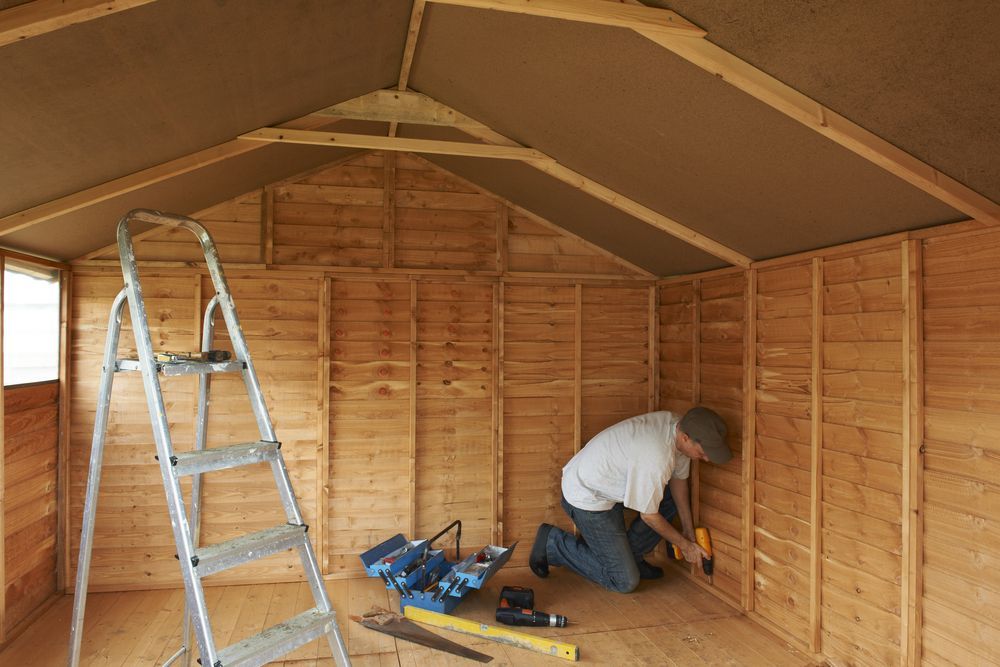 Man Inside a Wooden Shed, Kneeling and Using a Drill — Carl Whelan Building & Renovations In Lake Macquarie, NSW