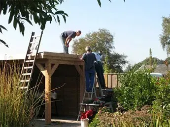 Twee mannen werken aan een houten constructie met een ladder