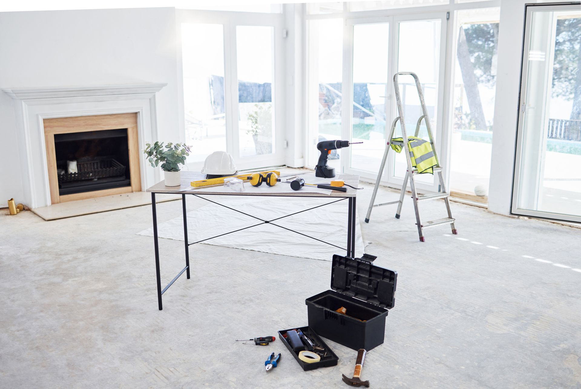 Bright living room under renovation with painting supplies, ladder, and a fireplace.