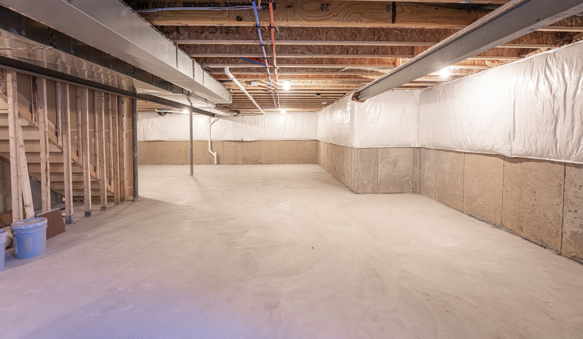 Unfinished basement with exposed beams, insulated walls, and a concrete floor under construction