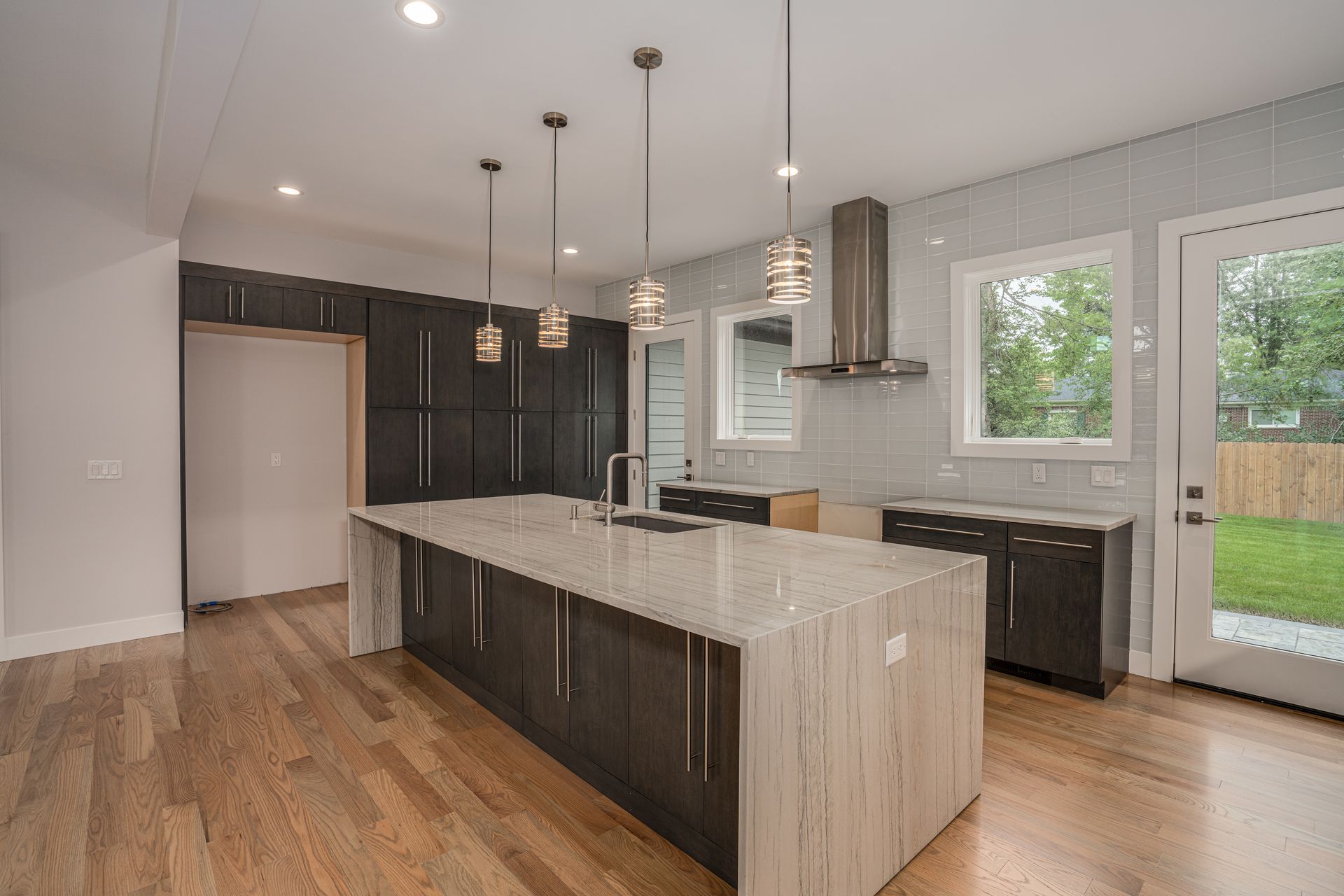 Modern kitchen with dark cabinets, large island, pendant lights, and sliding glass door to a yard.