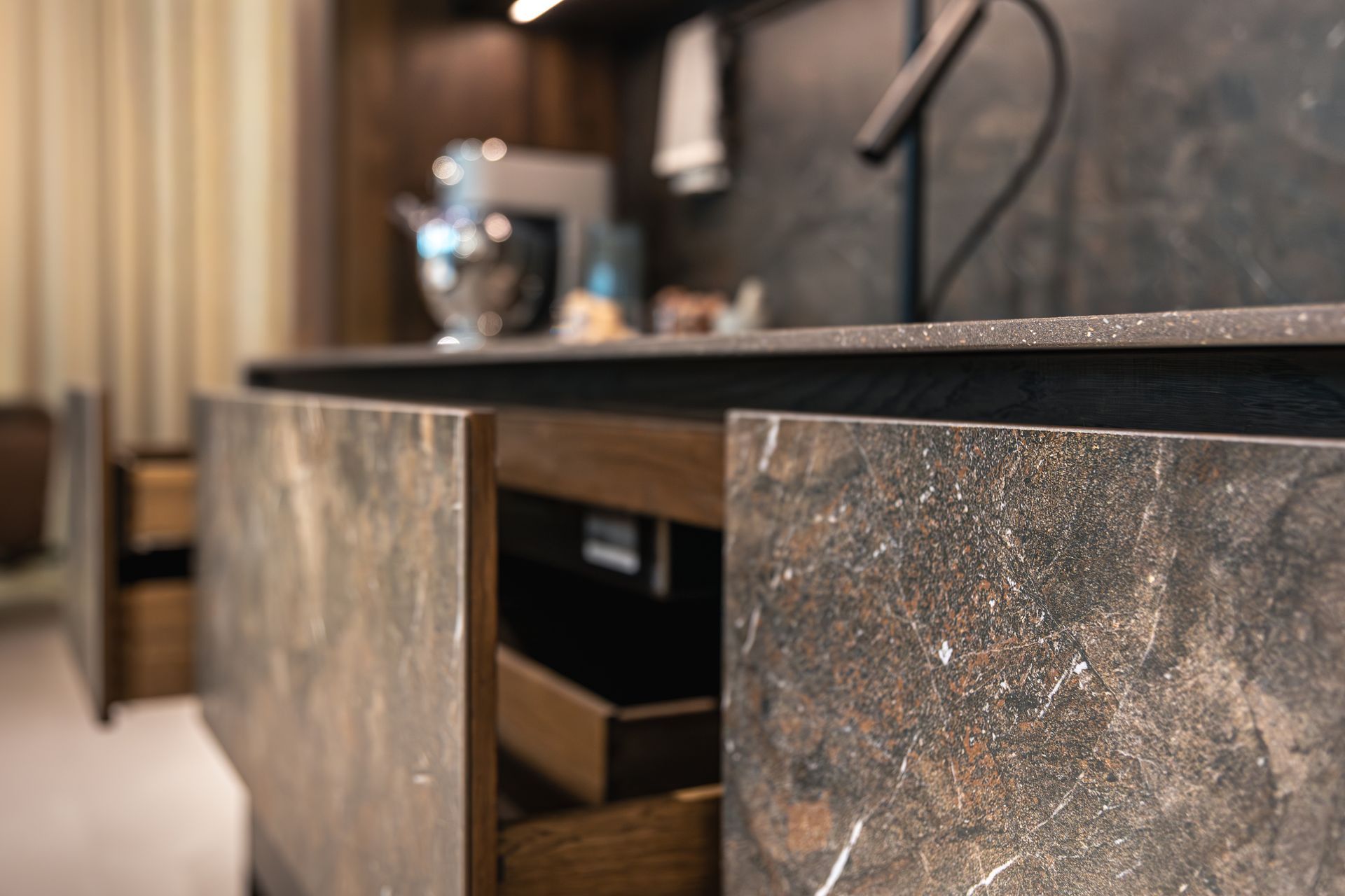 Stone-textured cabinet with an open drawer in a modern room, with a blurred chair and table lamp in the background