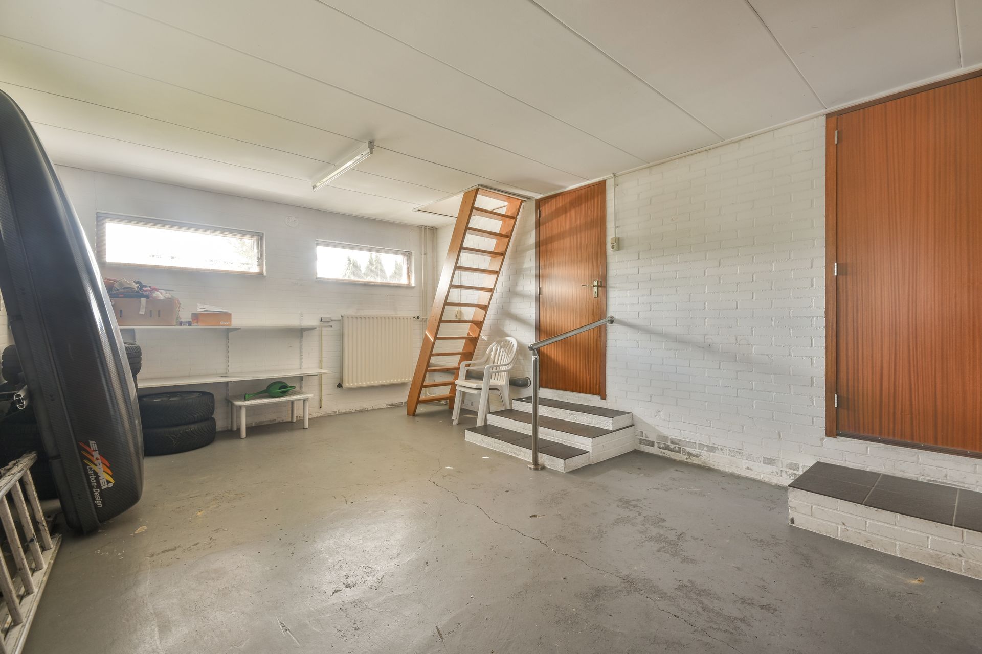 Garage interior with stairs, ladder, and windows, showing concrete floor and wood-paneled doors