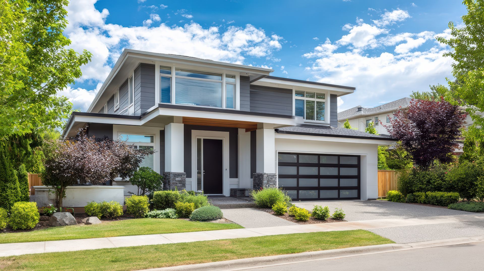 Modern two-story suburban house with a garage, landscaped front yard, and blue sky.