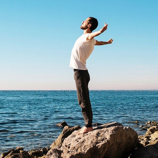 A man is standing on a rock near the ocean with his arms outstretched