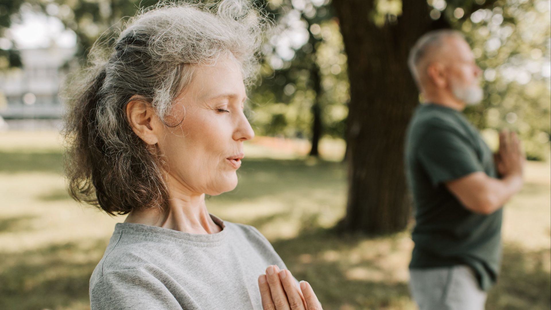 A man and a woman are practicing yoga in a park.