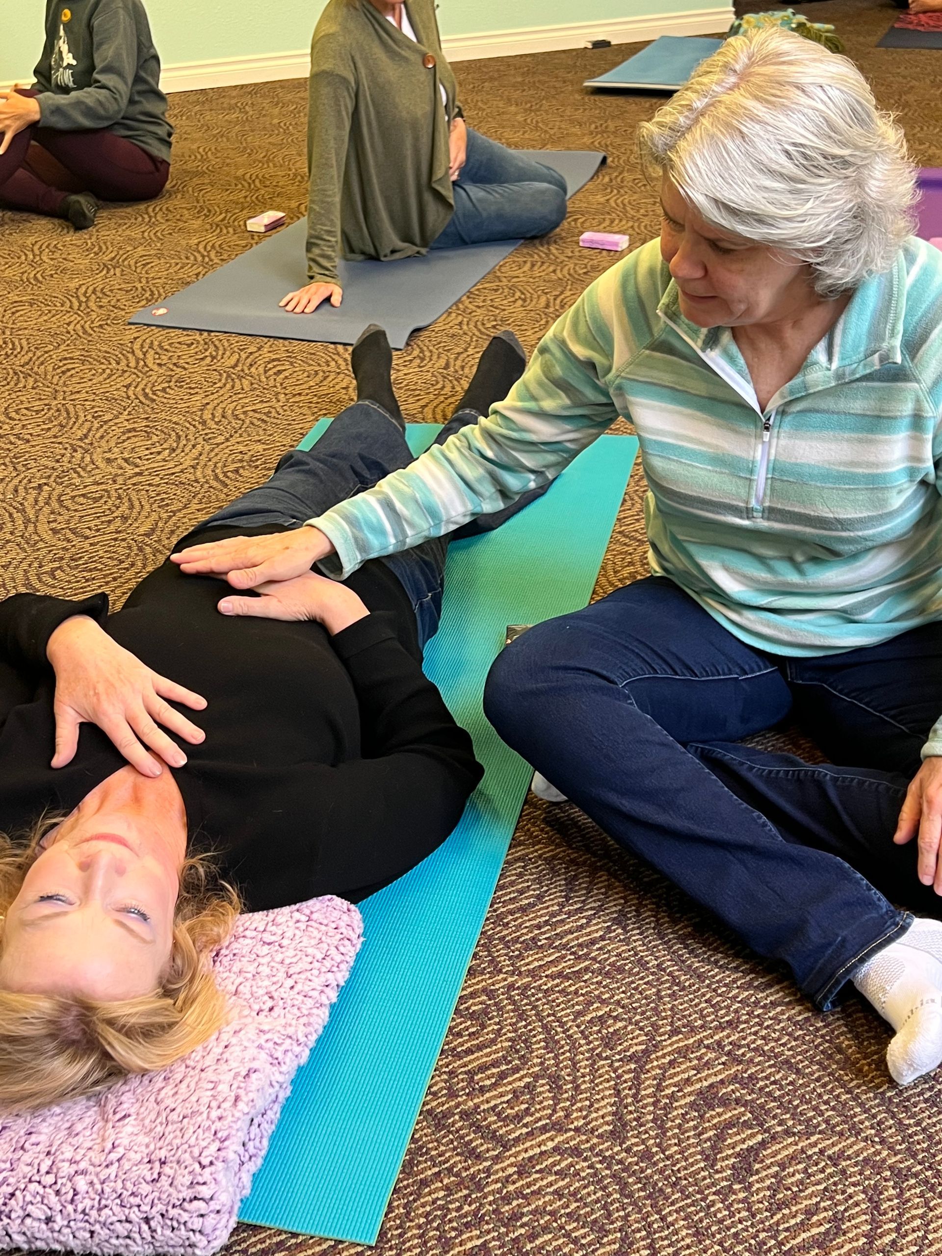 A group of women are sitting on yoga mats in a room.