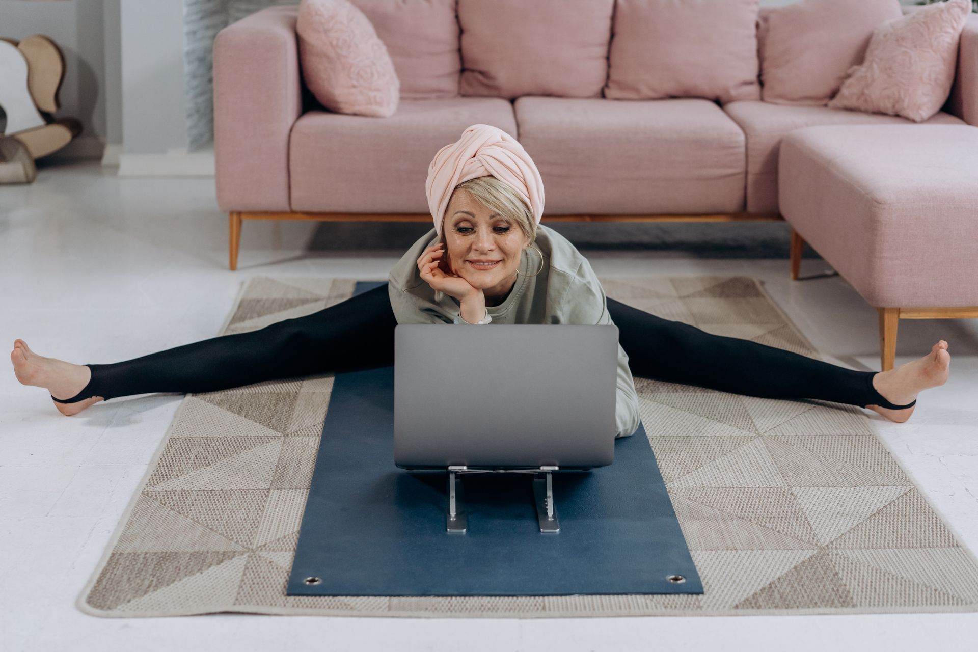 A woman is doing splits on a yoga mat while using a laptop.