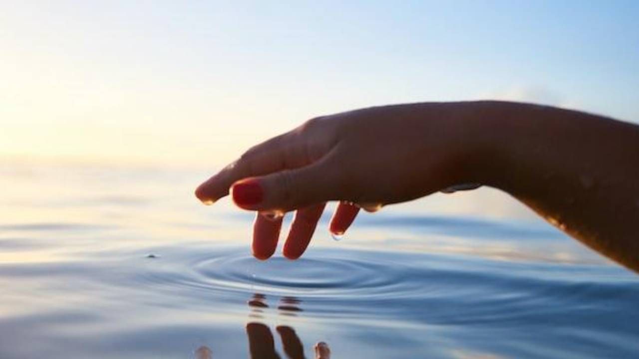 A woman 's hand is touching the water in the ocean.