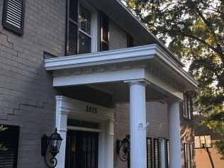 Two-story gray brick house with white porch and columns, black shutters, and two black sconces.