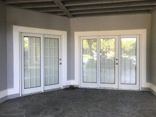 Gray patio with two sets of white-framed glass doors. The doors lead outside, reflecting trees.