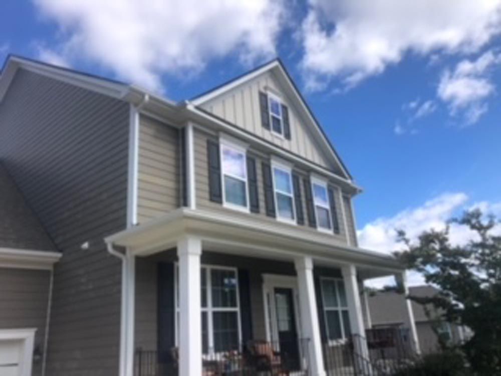 Two-story house with gray siding, white trim, porch, and blue sky with clouds.
