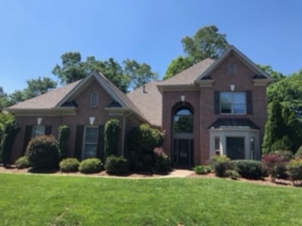 Brick house with green lawn and bushes under a blue sky.