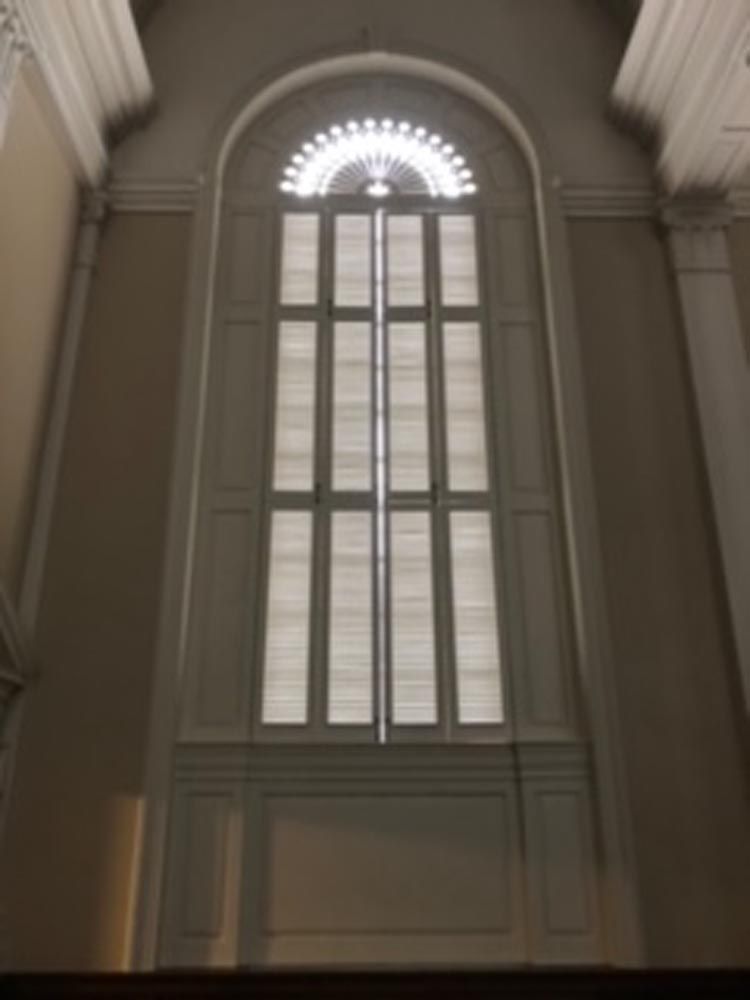 Tall arched window with white frame and blinds, in a cream-colored room.
