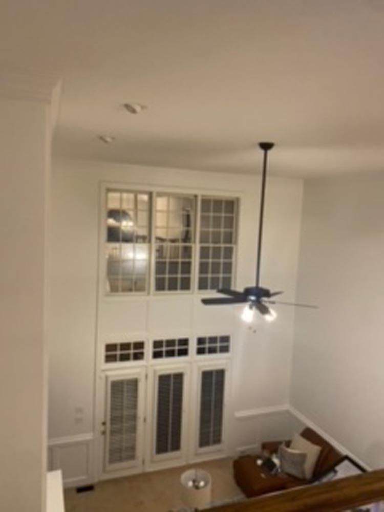 High ceiling interior with tall windows and a ceiling fan, looking down into a living space with a couch.