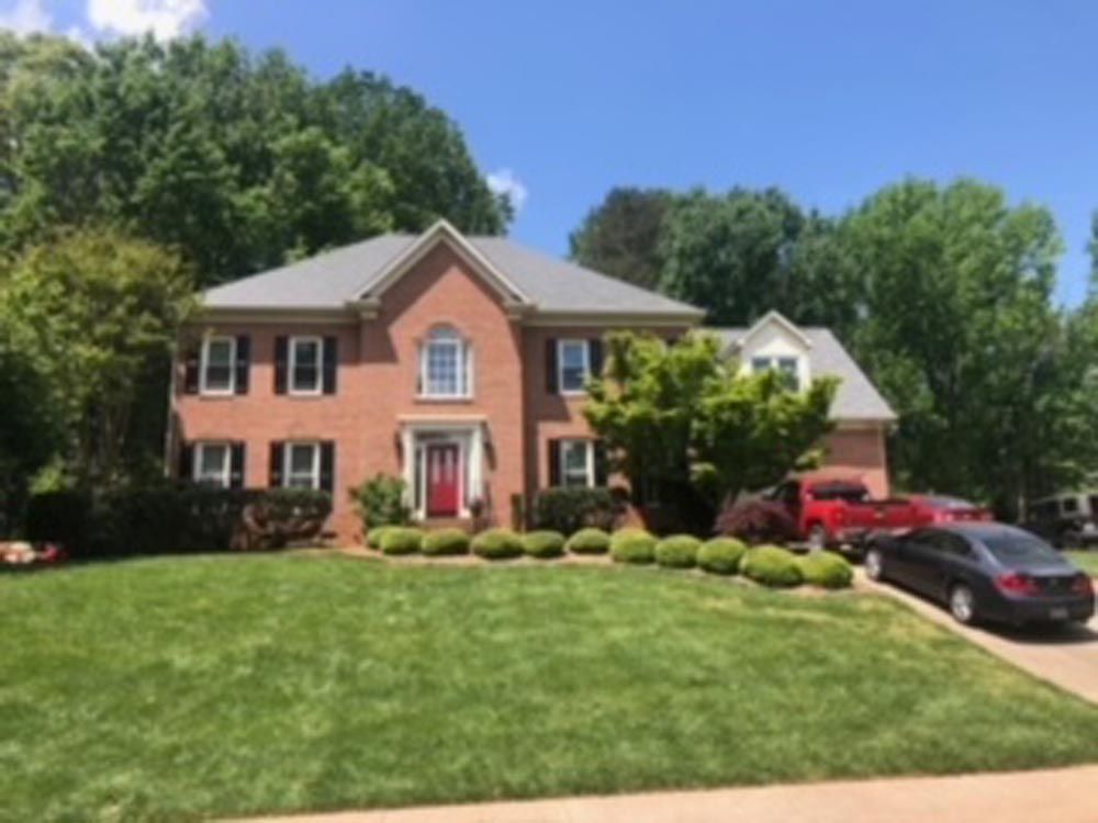 Two-story brick house with a red front door, black shutters, and well-manicured lawn on a sunny day.