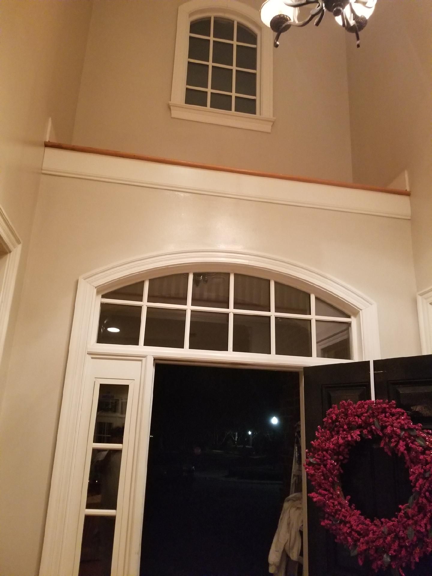 Interior view of a doorway with an arched window above, topped by a smaller square window, and a red wreath.