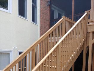 Wooden outdoor staircase ascending next to a beige building with windows and a brick wall.