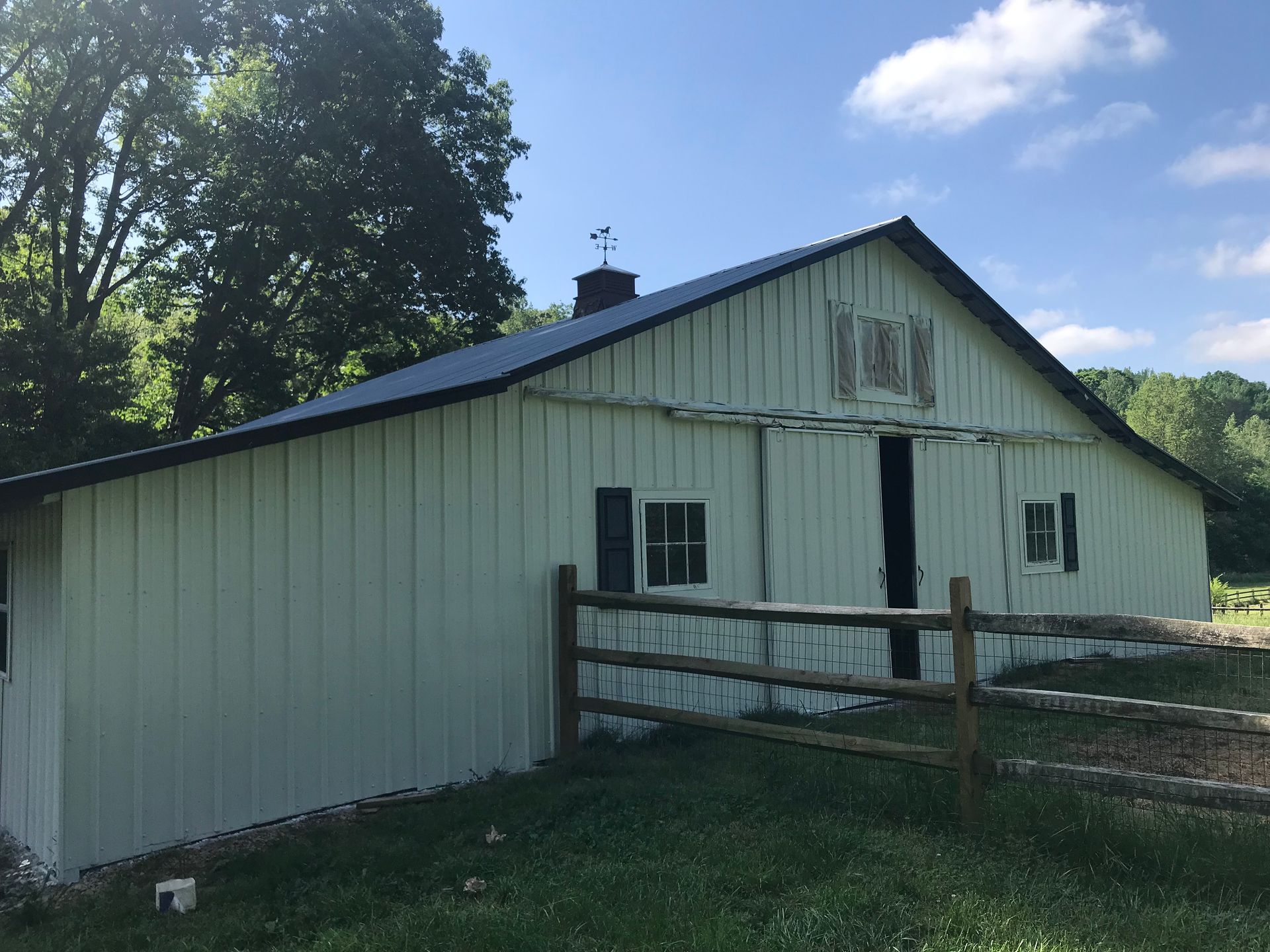 White barn with black roof, wooden fence, and open door on a sunny day.