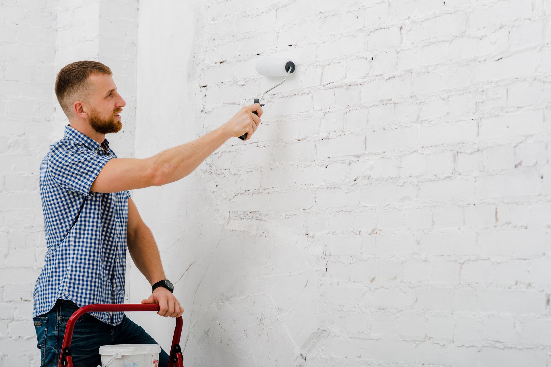 Man paints white brick wall with roller.