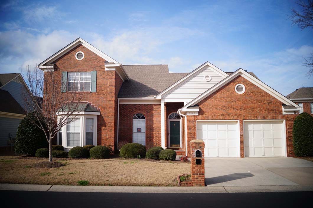 Brick house with white garage doors, a blue sky, and a front yard with bushes.